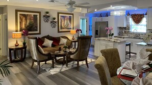 Un salon spacieux comprenant un canapé, des fauteuils et une table basse. Il y a également un coin cuisine avec un réfrigérateur et une table à manger dressée pour le repas.