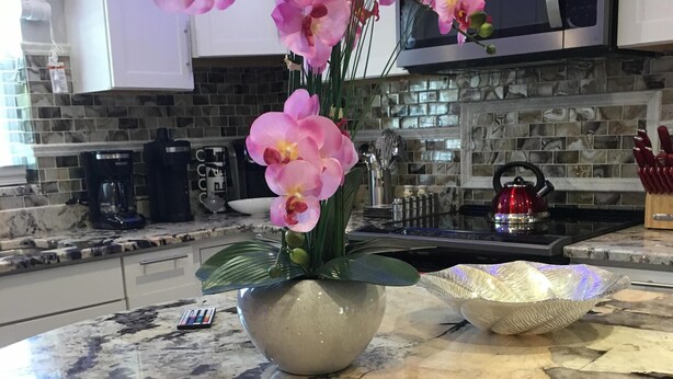 Une cuisine dotée d’un plan de travail en marbre, d’un four à micro-ondes, d’une bouilloire et d’un vase contenant des orchidées roses.