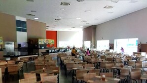 Una cafetería amplia con numerosas mesas y sillas, un mostrador con productos alimenticios y un ventanal que proporciona luz natural.