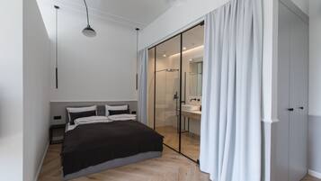 A modern bedroom with a large bed, a walk-in closet, and a glass shower area.