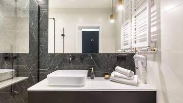 A modern bathroom with a large white sink, black marble tiles, a handheld showerhead, and a hairdryer on the counter.