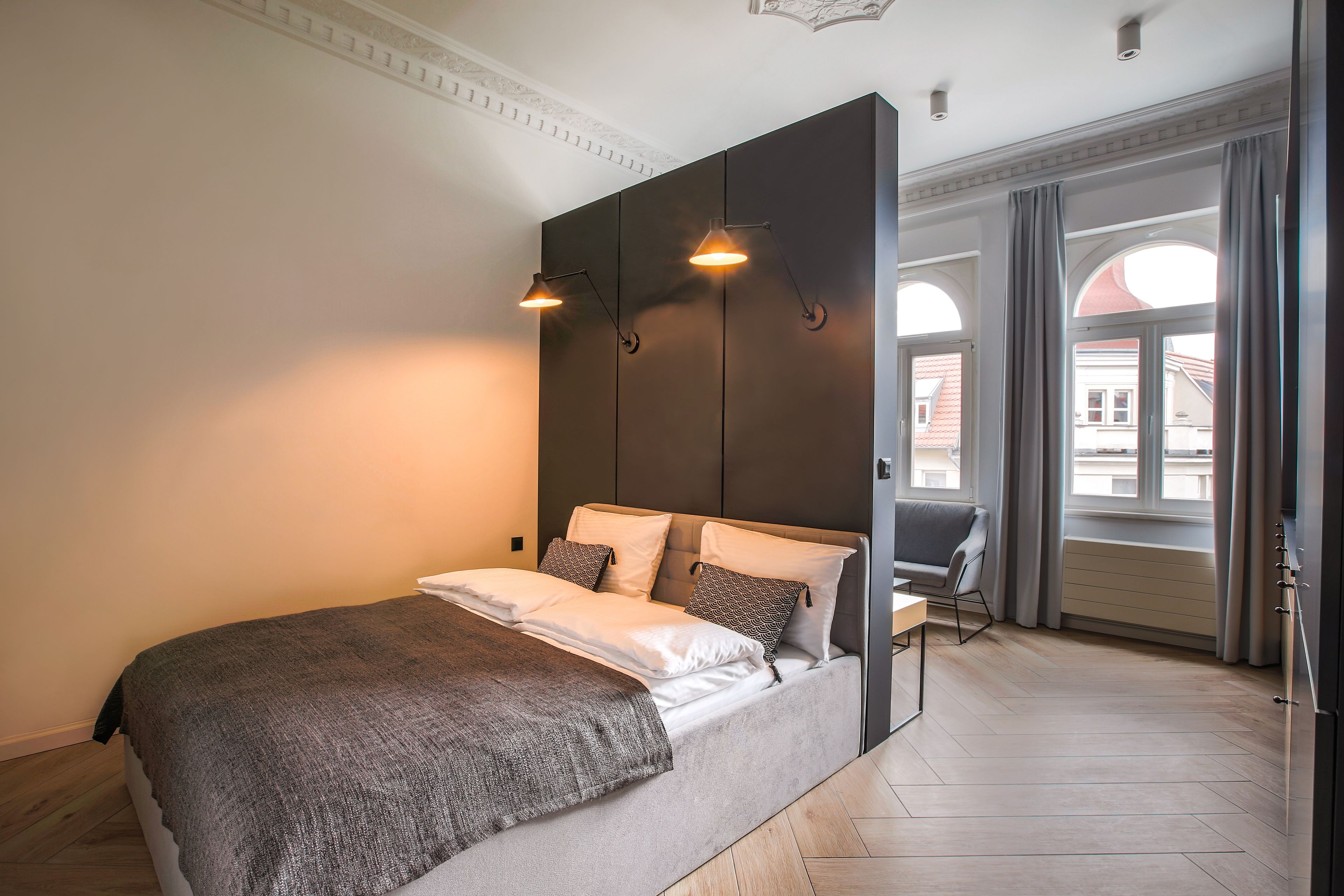 Un dormitorio moderno con una cama grande, un cabecero oscuro y vistas de la ciudad a través de amplias ventanas.