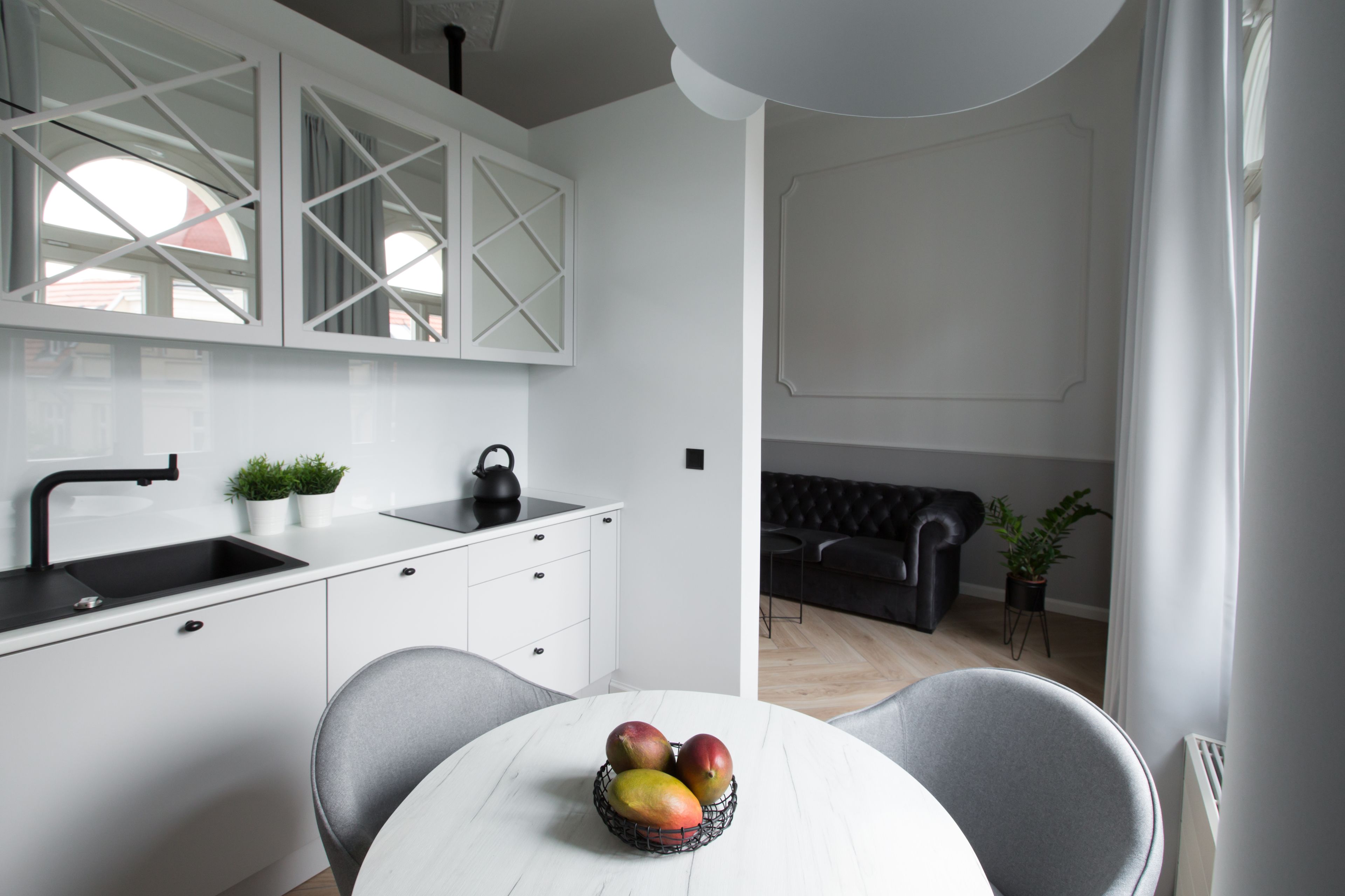 A modern kitchen with white cabinets, a black sink, and a round table with a fruit bowl.