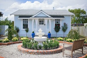 A light blue house with a white front porch, a central fountain, and a bench.