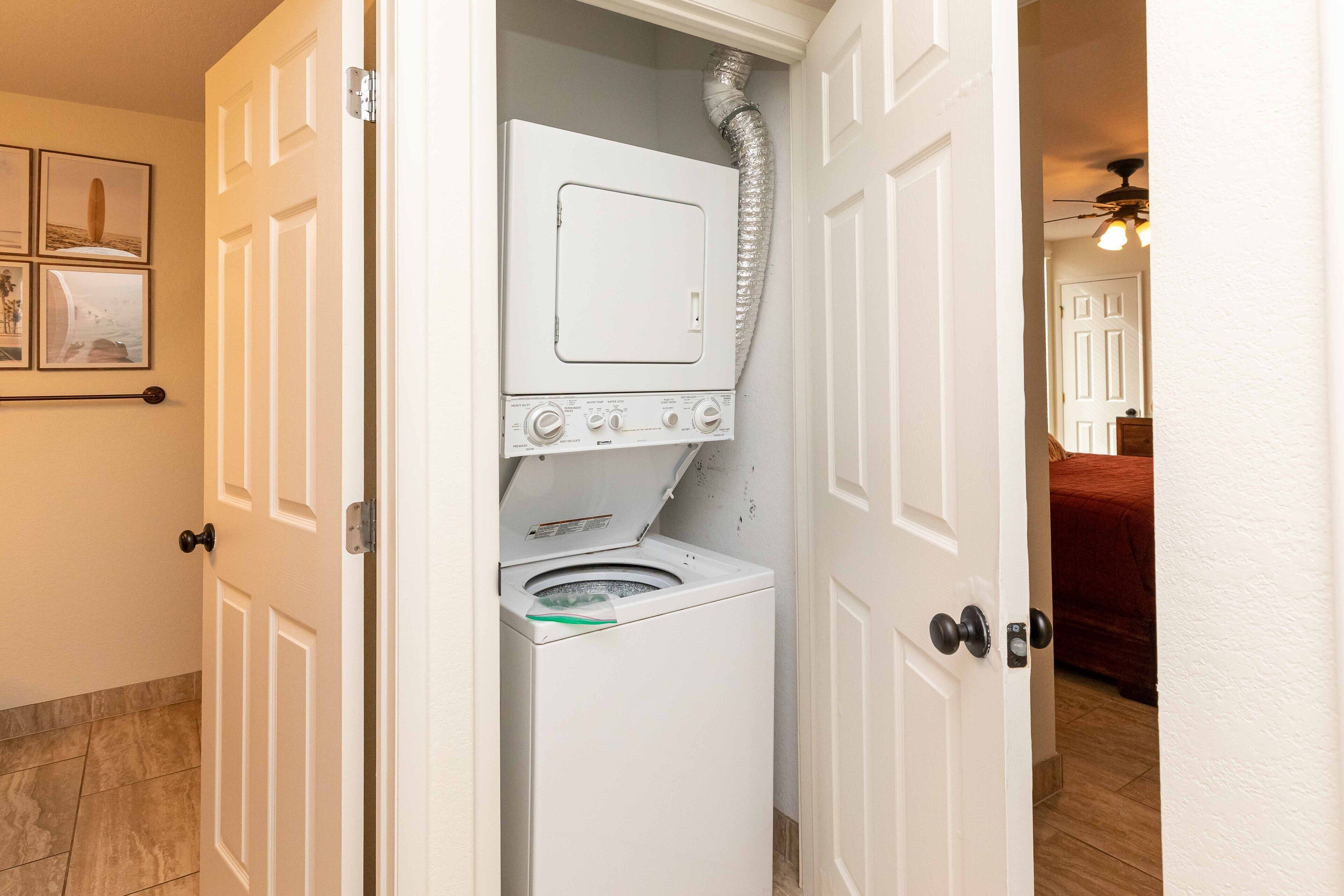A laundry room with a front-loading washer and dryer, a door with a metal handle, and a wall-mounted vent.