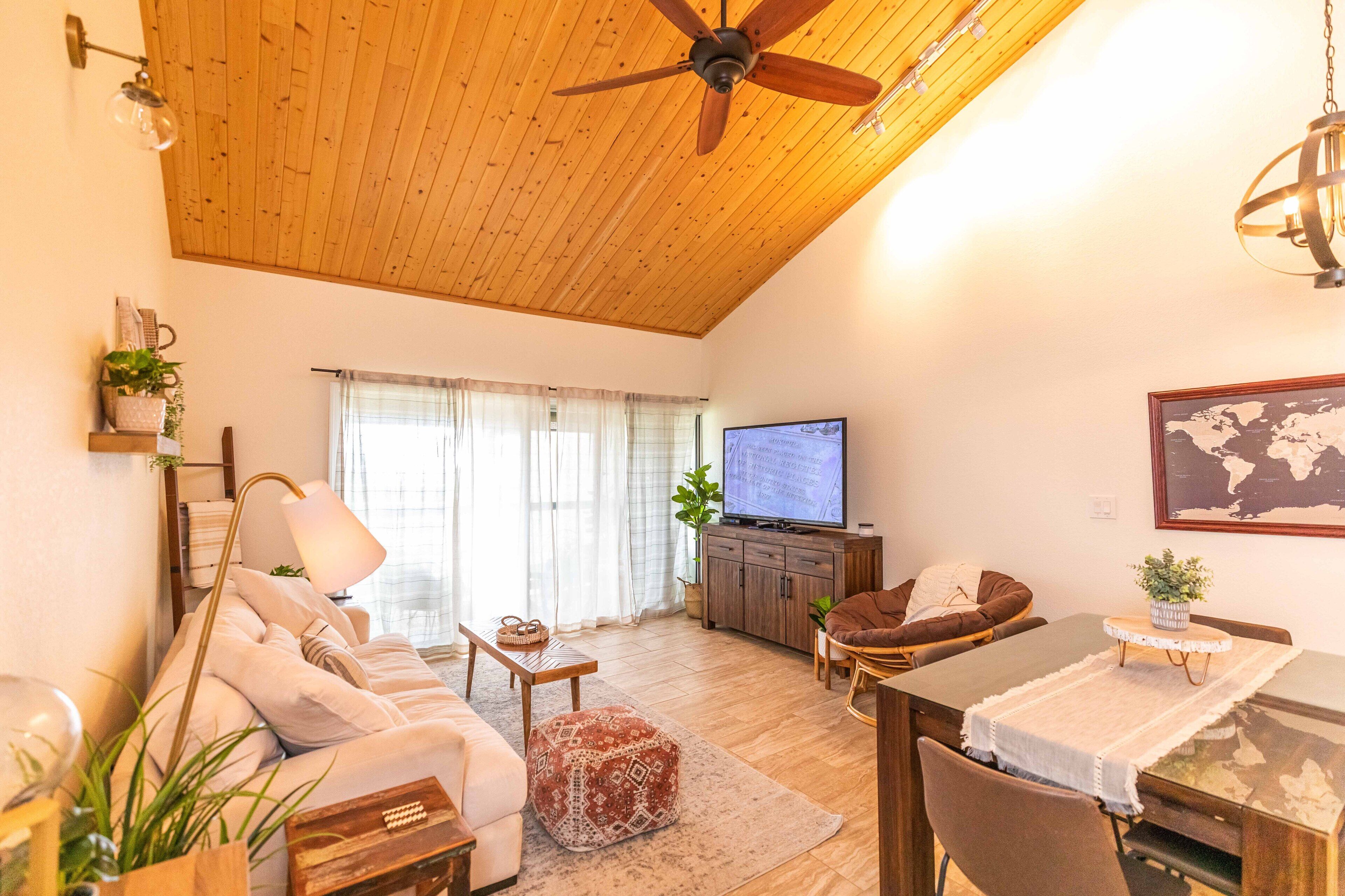 A cozy living room with a wooden ceiling, a sofa, a TV, and a dining area.