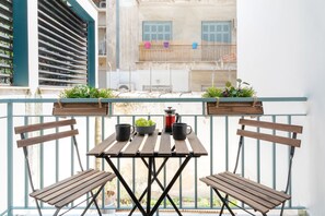 Un balcon avec une table en bois et deux chaises, une machine à café et un saladier de raisins.