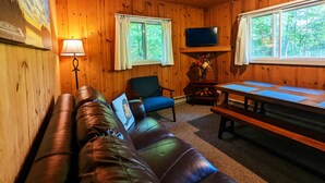 A cozy cabin interior with a leather couch, a wooden table, and a TV mounted on the wall.