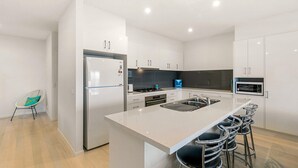 Een moderne keuken met witte kasten, een centraal eiland met barstoelen, een ingebouwde oven en een roestvrijstalen koelkast.