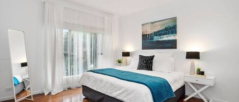 A modern bedroom with a large bed, white walls, and a painting above the bed.
