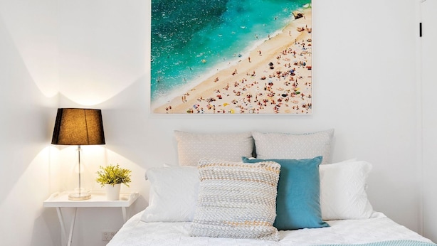 Une chambre à coucher avec un lit, des oreillers, une table de chevet avec une lampe, une petite plante et une décoration murale sur le thème de la plage.