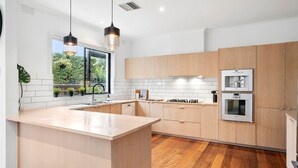 Une cuisine moderne avec des meubles en bois, un grand îlot central, des appareils électroménagers en acier inoxydable et des luminaires suspendus.