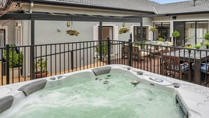 Un bain à remous dans un jardin, avec un espace patio, un coin salon abrité et une maison avec un toit en tuiles.