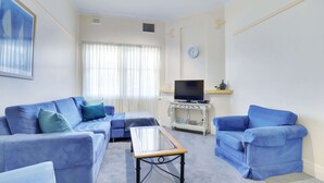 A living room with a sofa set, a coffee table, a television on a stand, and a clock on the wall.