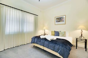 Un dormitorio con una cama, dos mesitas de noche con lámparas, una ventana con cortinas y un cuadro en la pared.