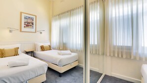 A hotel room with two beds, a small table, a wall-mounted picture, and a sliding glass door with curtains.