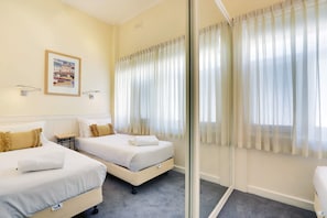 Camera d'albergo con due letti, un tavolino, un quadro appeso al muro e una porta finestra con tende.