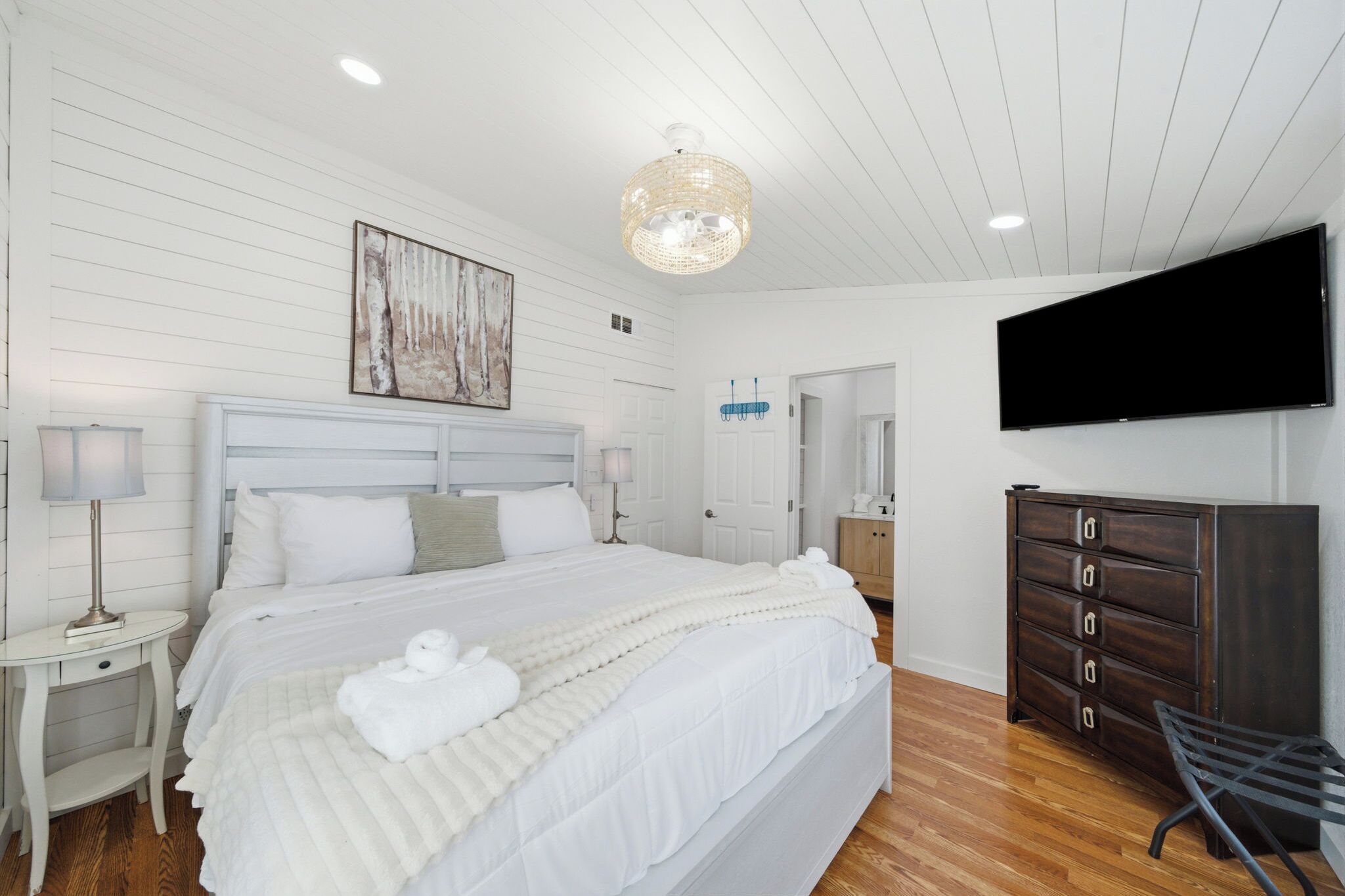 A bedroom with a bed, a dresser, a television, and a painting on the wall.