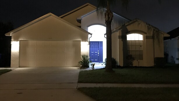 A residential house at night with a garage, a front door, and a palm tree.