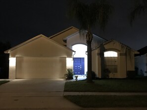 A residential house at night with a garage, a front door, and a palm tree. - Renovated Waterfront 3Bd/2B Home 20min to Disney, Universal and Shops (Kissimmee)