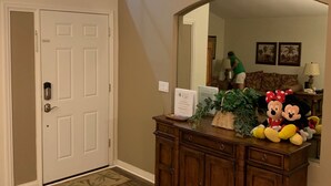A spacious entryway with a wooden floor, a large mirror, and a cabinet with plush toys.