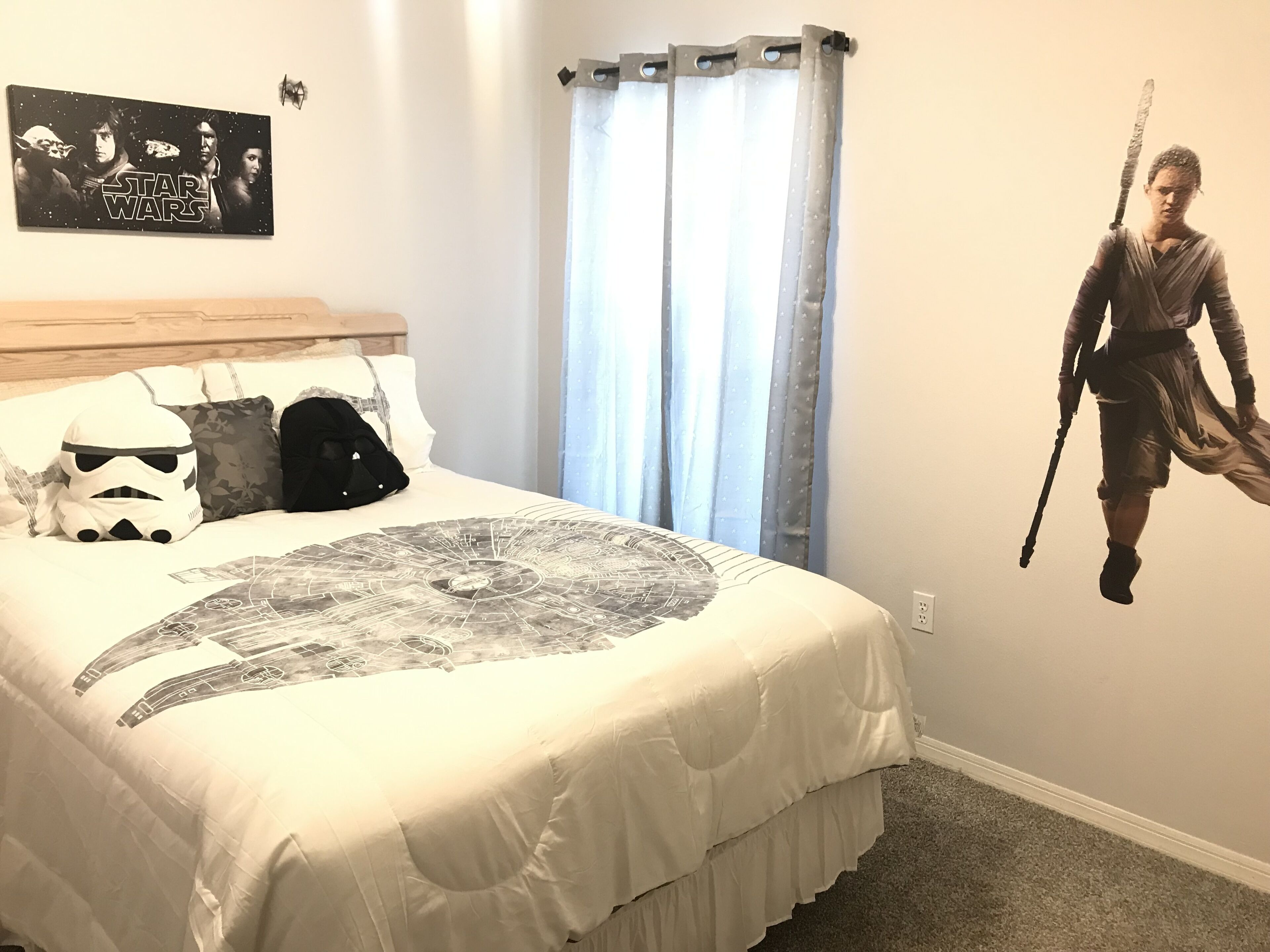 Ein Schlafzimmer mit Star Wars-Dekor, darunter eine Wandsticker mit einem Charakter, der ein Lichtschwert hält, ein Bett mit einer himmelsszogenen Bettdecke und ein Star Wars-Poster an der Wand.