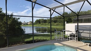 A pool area with a view of a lake, surrounded by a covered patio with chairs and a table.