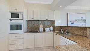 Une cuisine moderne avec des meubles blancs, un plan de travail en granit, un four encastré, un four à micro-ondes, un grille-pain et un évier.