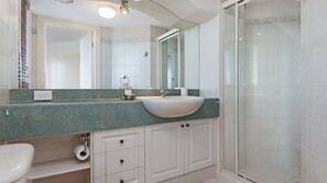 Ein Badezimmer mit einem weißen Waschbecken, einem Spiegel, einer Dusche mit Glastür und einer grünen Marmorarbeitsplatte.
