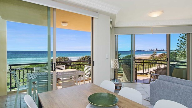Un balcon avec vue sur l’océan et la plage, un coin repas avec une table et des chaises, et une grande porte-fenêtre coulissante.