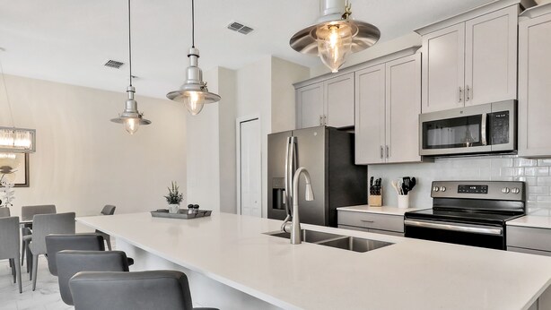 Una cocina moderna con una isla grande, electrodomésticos de acero inoxidable e iluminación colgante.