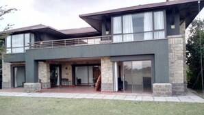 A modern two-story house with a stone facade, large sliding glass doors, and a flat roof.