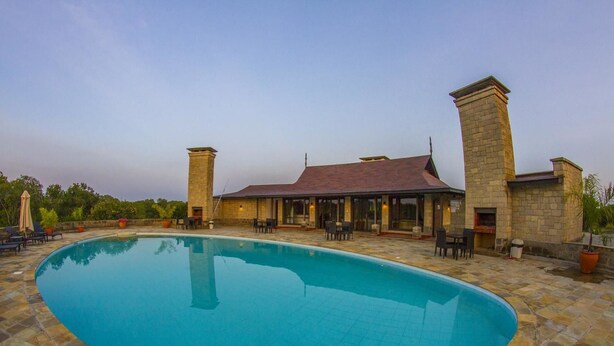 A swimming pool with a stone patio, a covered outdoor seating area, and a building with a red roof.