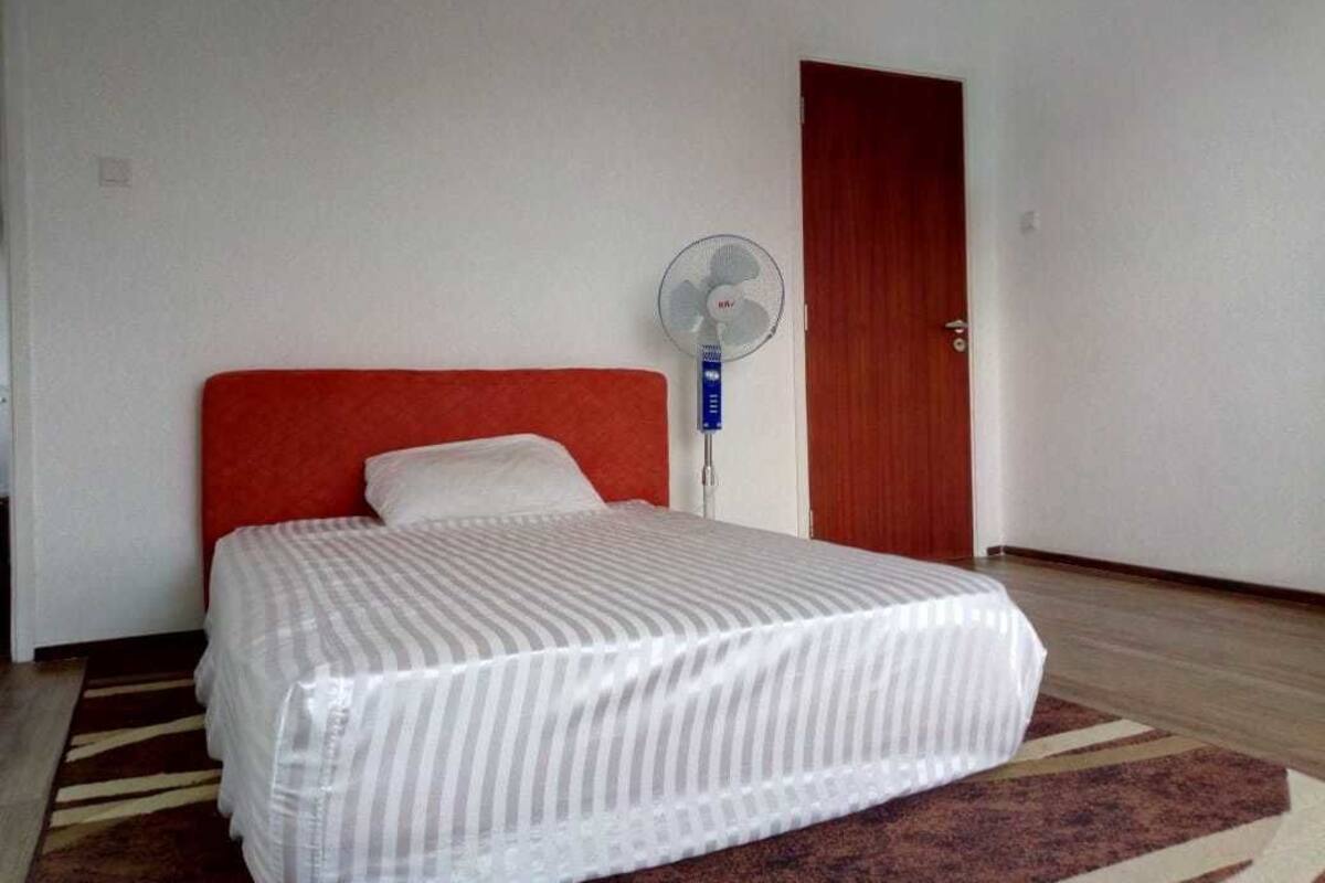 Ein Hotelzimmer mit einem Bett, einem Standventilator und einer Holztür.