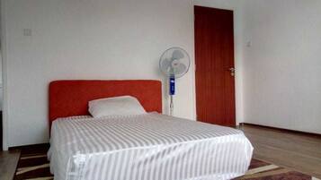 A hotel room with a bed, a standing fan, and a wooden door.