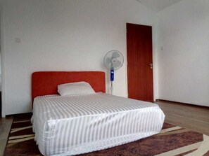 Una habitación de hotel con una cama, un ventilador y una puerta de madera.