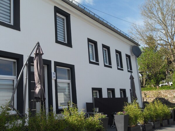 A white building with black window frames and shutters, outdoor seating, and a satellite dish. - Gästehaus Nettes Landhaus (Winterspelt)
