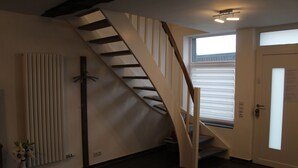 Eine Treppe mit Holzbalken und einer weißen Wand, an der ein Heizkörper und eine Tür mit Milchglas eingelassen sind.