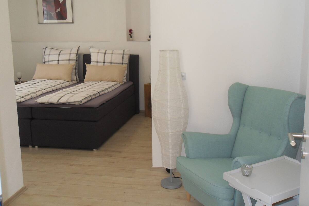 Un dormitorio con cama, mesita de noche, lámpara y silla.