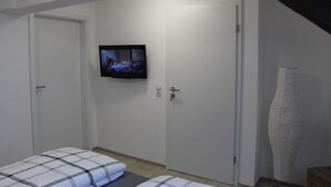 Ein Schlafzimmer mit einem Bett, einem an der Wand befestigten Fernseher und einer Tür.
