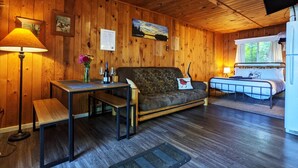 A cozy cabin interior with wooden walls, a dining table with a bench, a sofa, a bed, and a mounted TV. - Amenities & Resort Access Included, Cabin 11 (Phelps)
