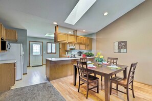 A modern kitchen with wooden cabinets, a central island, and a dining area with chairs. - Elwood Townhome w/ Patio - 7 Mi to Johnson Lake (Elwood)