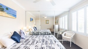 A hotel room with two beds, a large mirror, a ceiling fan, and a view of the beach through the window.