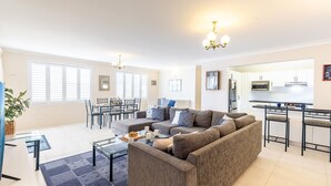 A modern living room with a grey sofa, a glass coffee table, and a dining area with a table and chairs. There is a kitchen with white cabinets and a stainless steel refrigerator. - Laman Lodge, 6,15 Laman Street - Air Conditioned unit with spectacular views and free Wi-Fi (Nelson Bay)