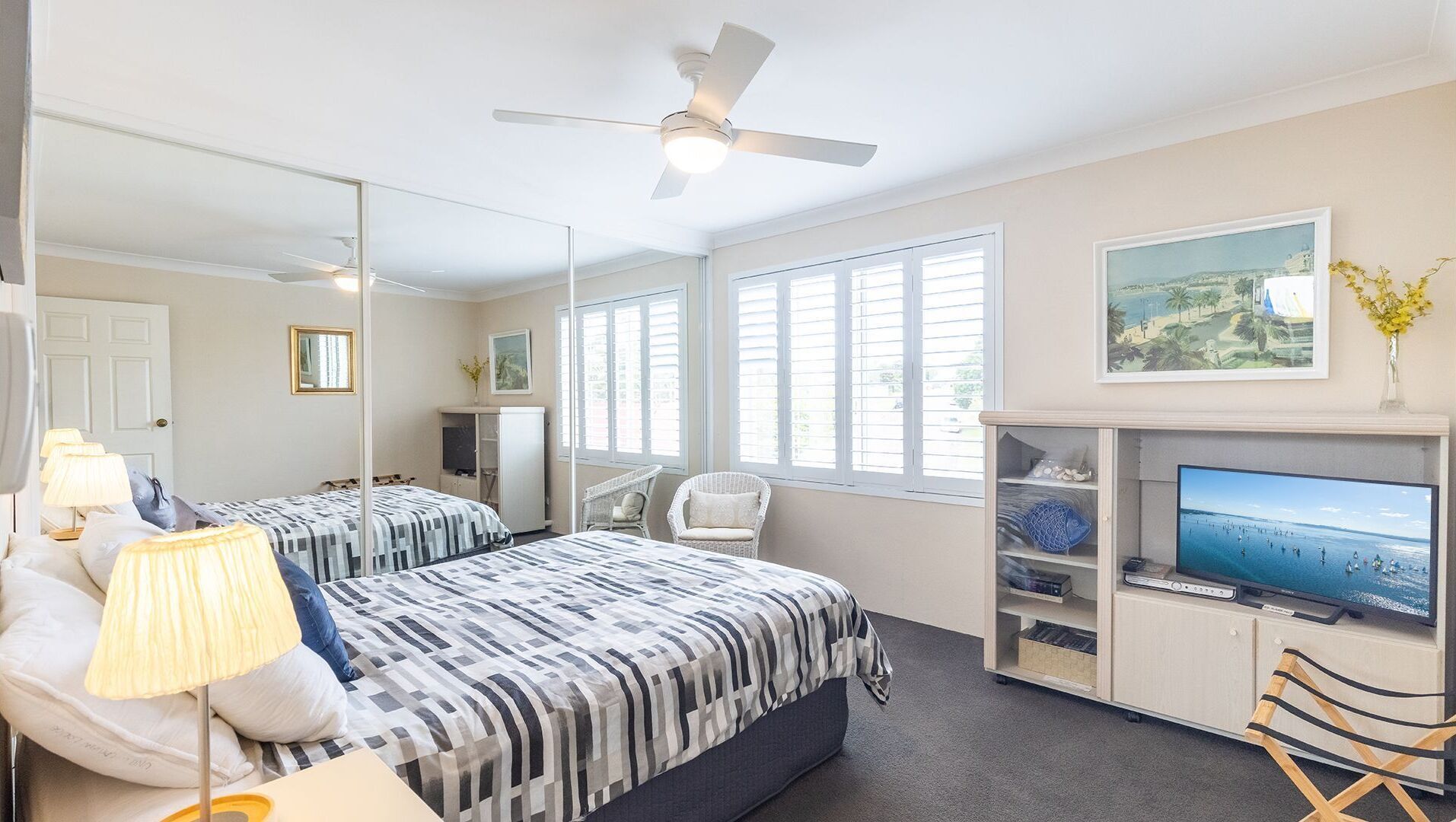 A bedroom with two beds, a ceiling fan, a TV, and a large window.
