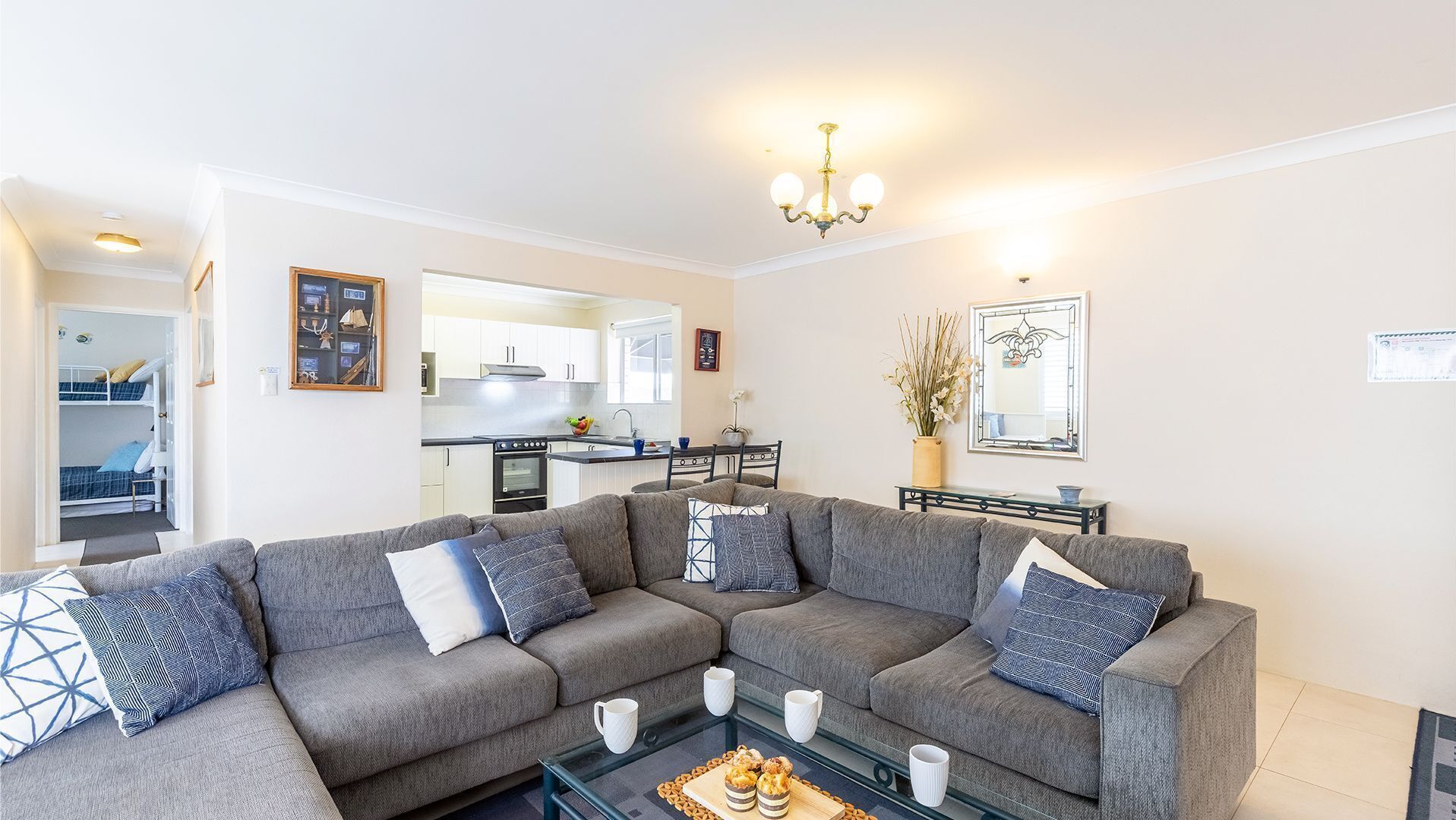 A modern living room with a sectional sofa, a glass coffee table, and a kitchen in the background.
