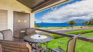 A balcony with wicker furniture, a view of the ocean, and a sign reading "Live Aloha".