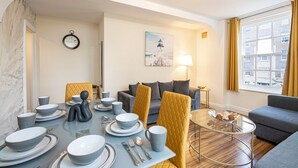 A modern dining area with a table set for four, a sofa, and a lamp. - Nice 3 Bedrooms Apartment Near Hyde Park & Oxford St (London)