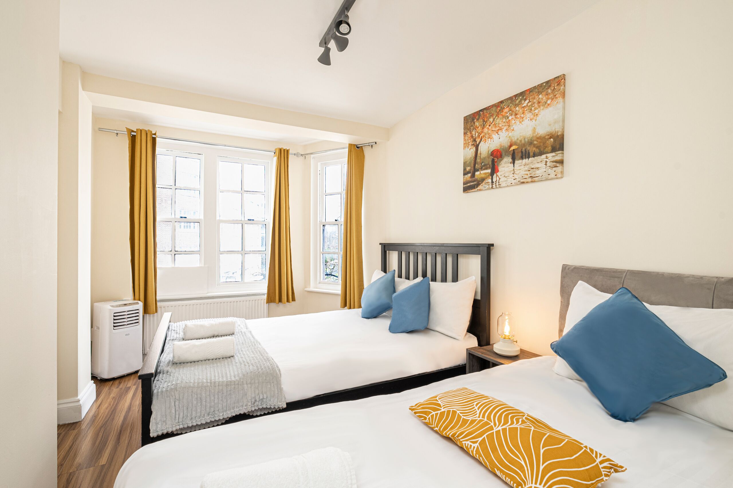 Camera d'albergo con due letti, un termosifone, una finestra con tende e un quadro appeso al muro.