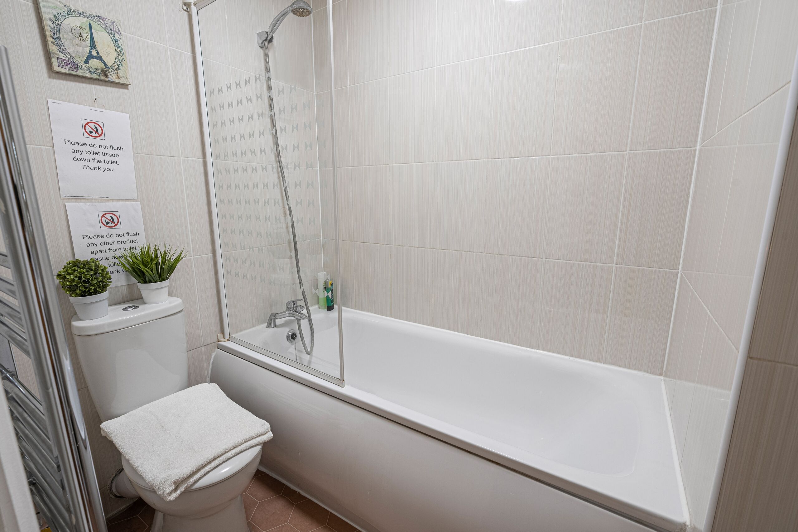 A bathroom with a toilet, a shower, and a bathtub. There are signs on the wall and a small plant on the toilet.